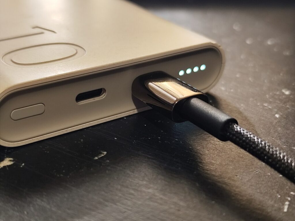 USB-C cable plugged into a power bank beside its illuminated charge indicators.